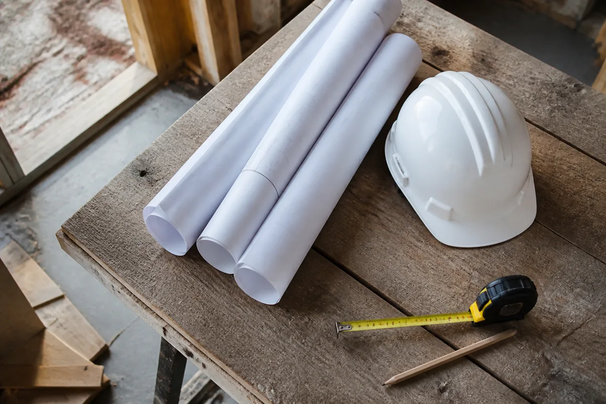 Plans de construction enroulés et casque de chantier posés sur une table en bois